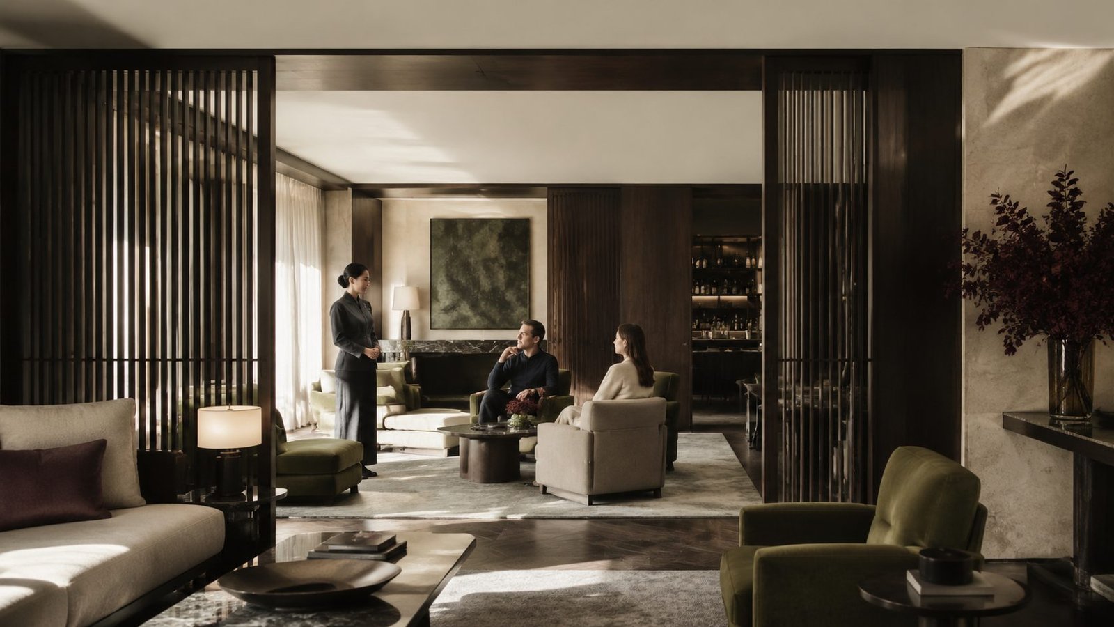 Screened hotel lounge with separated seating areas and a staff member attending two guests